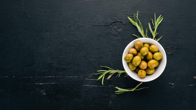 Olive in un piatto e rosmarino Su uno sfondo di legno nero Spazio libero per il testo