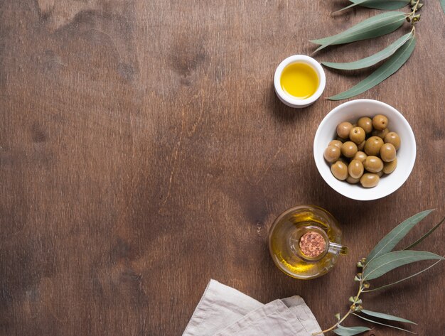 Olive naturali mature con olio in una bottiglia su un fondo di legno marrone