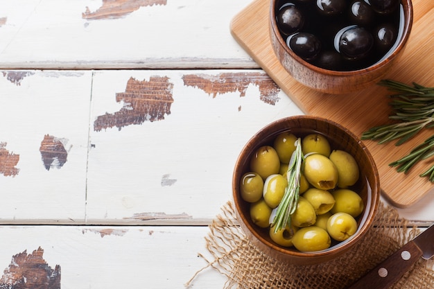 Olive nere e verdi in ciotole di legno sulla tavola di legno. Vista dall'alto con spazio per il testo.