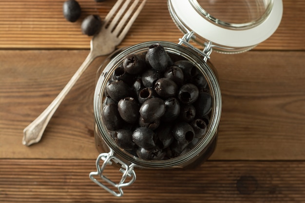 Olive nere snocciolate sottaceto in barattolo di vetro, fondo di legno. Cibi mediterranei Copia spazio