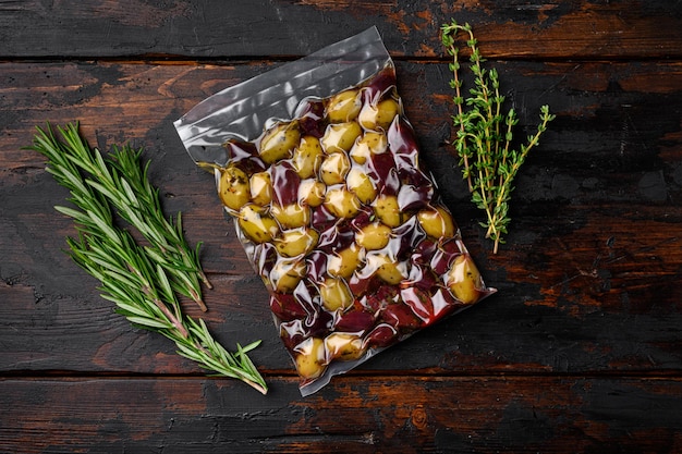 Olive verdi e nere in confezione, su vecchio sfondo di tavolo in legno scuro, vista dall'alto piatta, con spazio di copia per il testo