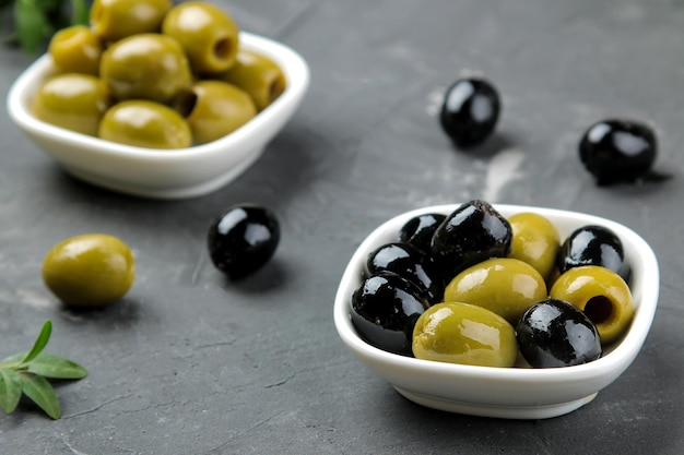 Olive verdi e nere in una ciotola di ceramica bianca con foglie su uno sfondo di grafite scuro. avvicinamento