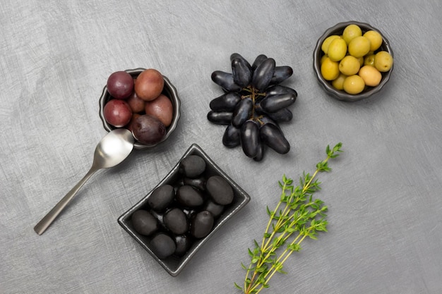 Olive verdi rosse e nere in ciotole Rametto di timo e un grappolo d'uva nera