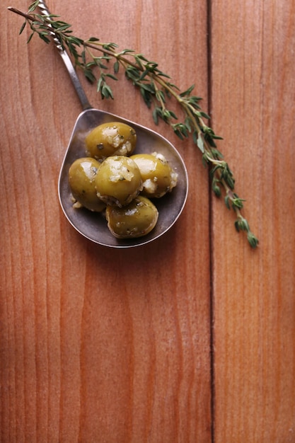 Olive verdi sott'olio con spezie e rosmarino in cucchiaio su tavola di legno