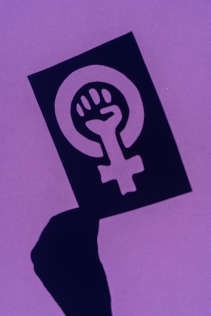 Ombra del simbolo della lotta per il femminismo su sfondo viola, pugno chiuso di una donna durante le proteste di marcia per i diritti delle donne, foto verticale