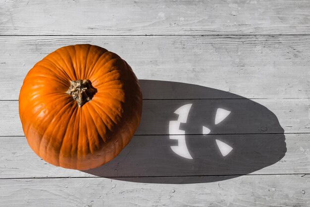 Ombra sorridente spettrale di una lanterna di zucca arancione su legno bianco vista dall'alto da vicino, Halloween desi