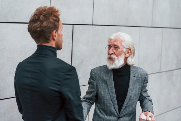 Ombrello e tazza di bevanda Giovane ragazzo con uomo anziano in abiti eleganti è insieme all'aperto Concezione del business