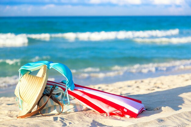 Ombrello rosso e bianco colorato con cappello di paglia, borsa da spiaggia e costume da bagno reggiseno bikini blu contro la spiaggia dell'oceano con bel cielo blu e nuvole