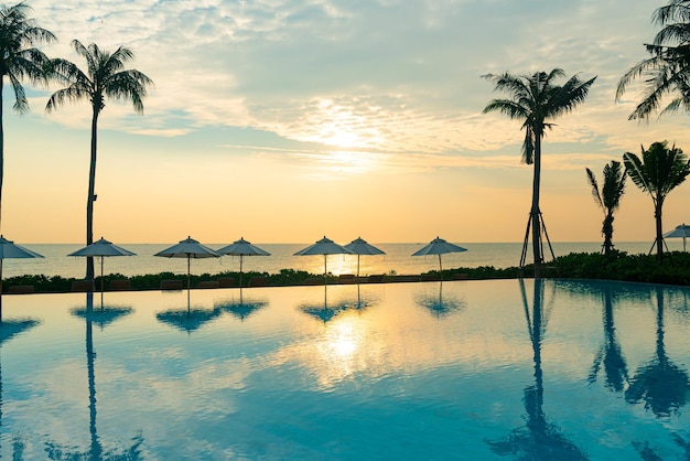 ombrellone con lettino piscina intorno alla piscina con sfondo del mare oceano al tramonto o all'alba - concetto di vacanza e vacanza