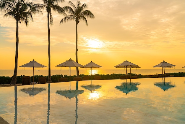 ombrellone con piscina intorno alla piscina con sfondo oceano mare al tramonto o all'alba - concetto di vacanza e vacanza