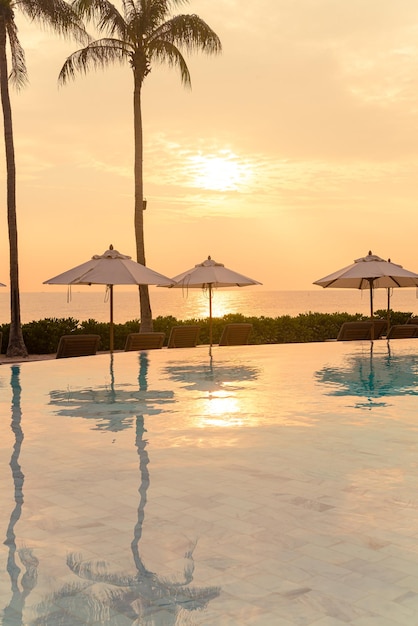 ombrellone con piscina intorno alla piscina con sfondo oceano mare al tramonto o all'alba - concetto di vacanza e vacanza