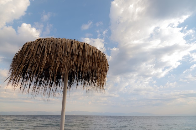 Ombrellone di paglia sulla spiaggia contro il cielo nuvoloso Grecia isola di Taso vacanze estive