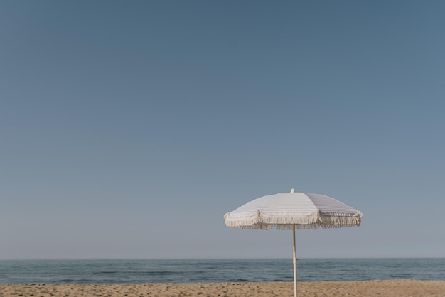 Ombrellone sulla spiaggia di sabbia di fronte al mare blu e al cielo Concetto minimo di vacanze estive