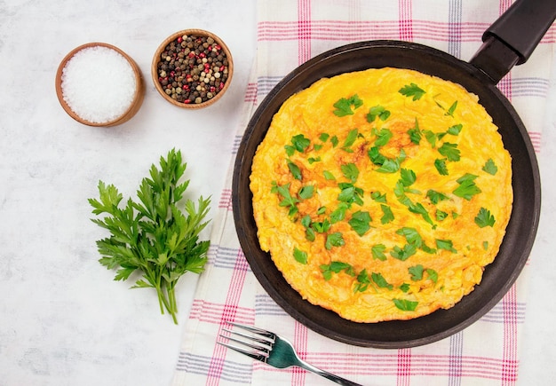 omelette con prezzemolo in una padella su uno sfondo grigio vista superiore