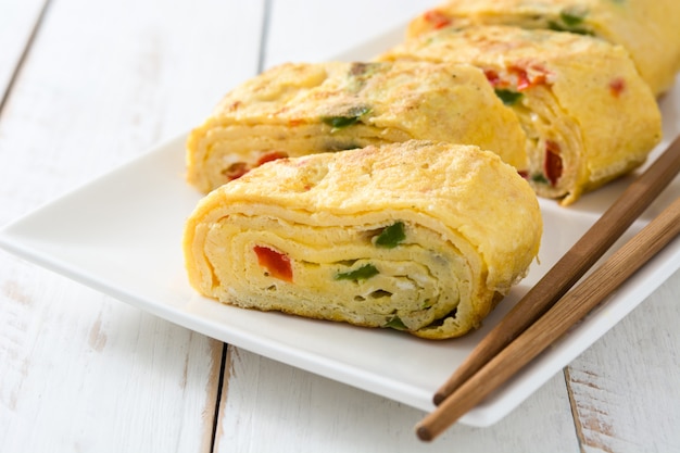 Omelette giapponese tradizionale di tamagoyaki sulla tavola di legno bianca.