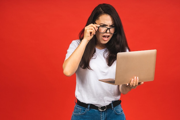 OMG Sono scioccato Ritratto di una donna d'affari giovane e bella scioccata azienda computer portatile isolato su sfondo rosso