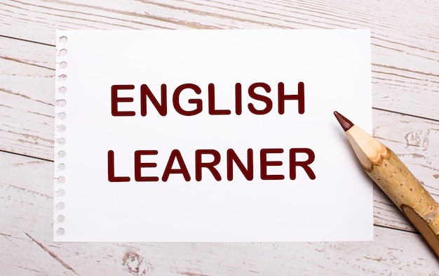 On a light wooden background a colored pencil and a white sheet of paper with the text ENGLISH LEARNER