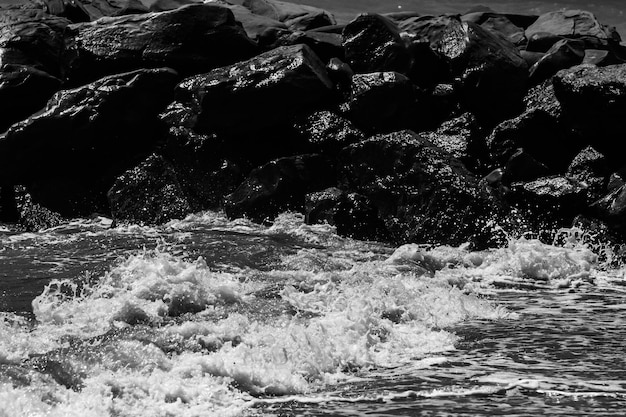 Onde del mare con schiuma e grandi pietre fotografia in bianco e nero della spiaggia