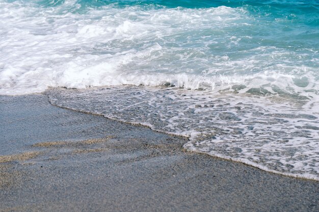 Onde spumose bianche sul primo piano della spiaggia sabbiosa. Al mare nella soleggiata giornata estiva. Concetto di tempo di vacanze estive.