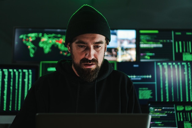 One criminal hacker man programming a phishing virus at background a lot of data screens One caucasian developer working on internet firewall system Cyber security concept