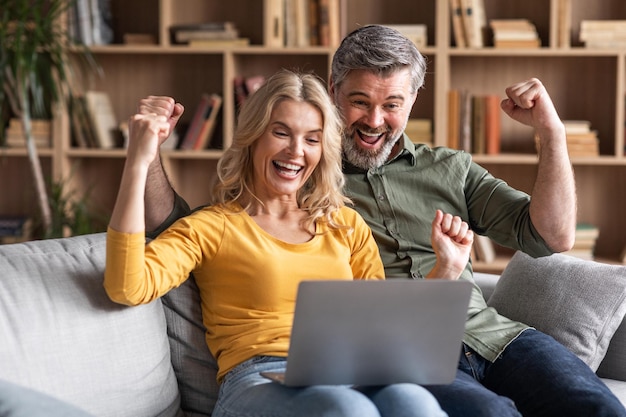 Online Win Ritratto di felicissima coppia di mezza età che celebra il successo con il laptop
