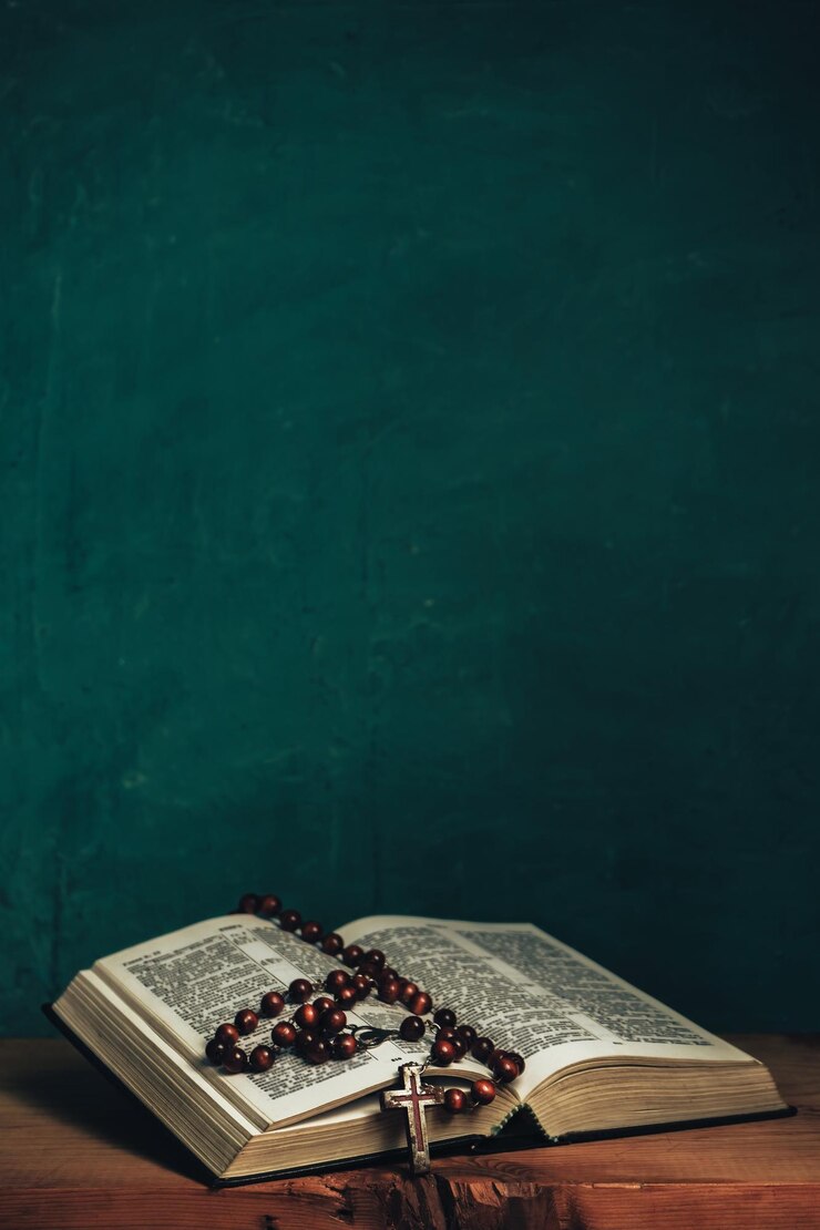 Open Holy Bible and beads crucifix on a red old wooden table Beautiful green wall background