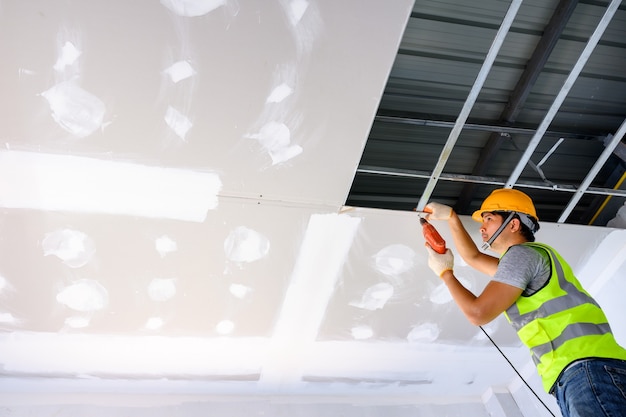 operai edili che indossano uniformi Installare il soffitto in gesso all'interno della casa e dell'edificio. Utilizzare un cacciavite elettrico per installare il soffitto.