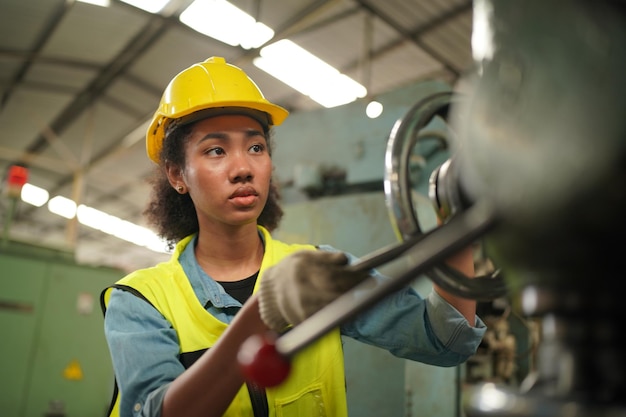 Operaia industriale femminile nell'elmetto con la fabbrica di produzione dell'industria pesante in background con varie parti di progetto di lavorazione dei metalli.Lavoro presso la fabbrica di produzione dell'industria pesante.