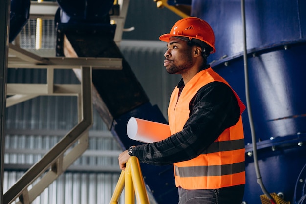 Operaio afroamericano in piedi in uniforme che indossa un cappello di sicurezza in una fabbrica