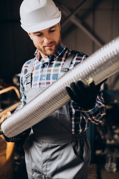 Operaio che indossa elmetto lavorando con tubo metallico in fabbrica