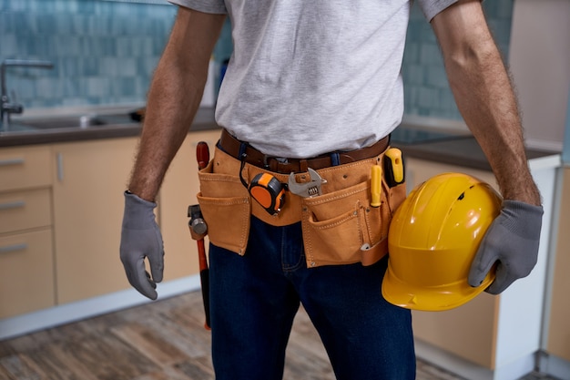 Operaio con cintura per strumenti e casco in piedi in cucina