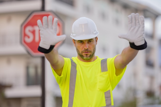 Operaio con segnale stradale di stop Costruttore con gesto di arresto nessuna mano pericolosa sul concetto di costruzione Uomo in uniforme da lavoratore e elmetto protettivo con mano aperta che fa il segnale di stop