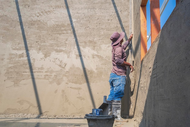 Operaio costruttore che utilizza una cazzuola lunga per lucidare il muro di cemento all'interno del cantiere della casa