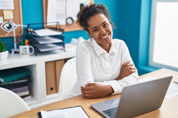 Operaio d'affari donna afroamericana che utilizza il computer portatile seduto con le braccia incrociate gesto in ufficio