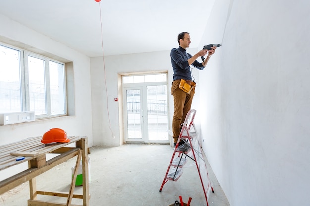 Operaio del costruttore con l'attrezzatura pneumatica del perforatore del martello pneumatico che fa il foro in parete al cantiere