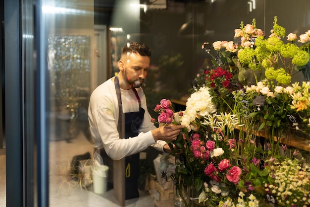 Operaio del negozio di fiori che raccoglie un bouquet nel frigorifero per i fiori appena tagliati