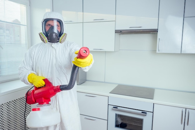 Operaio di controllo dei parassiti in piedi con lo spruzzatore in cucina