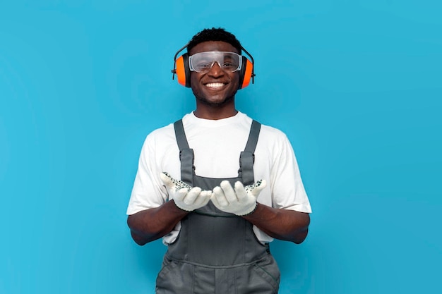operaio di costruzione maschio afroamericano in uniforme tenendosi per mano davanti a lui su sfondo blu