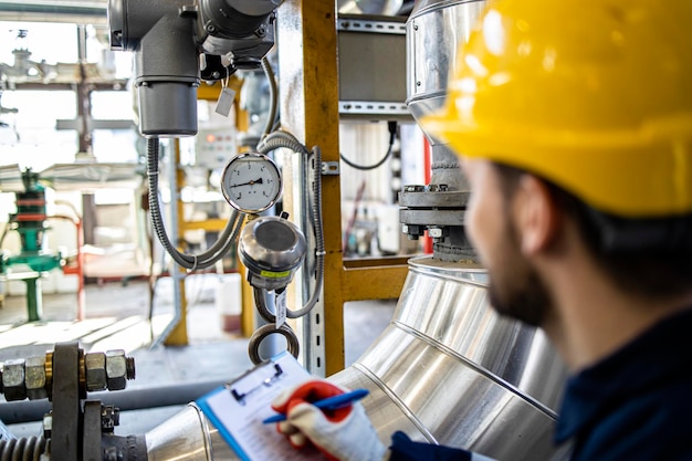 Operaio di fabbrica in uniforme di sicurezza che controlla il manometro degli impianti di gasdotti in raffineria