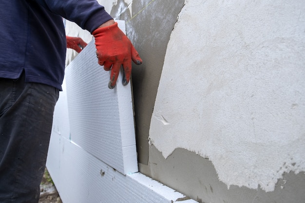 Operaio edile che installa fogli isolanti in polistirolo sulla parete della facciata della casa per la protezione termica.