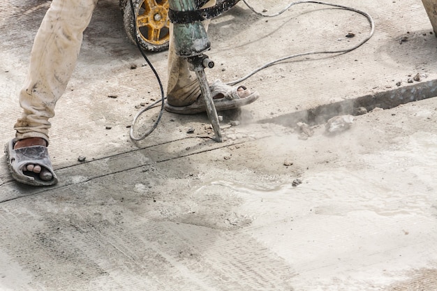 Operaio edile che utilizza la superficie del calcestruzzo di perforazione del martello pneumatico