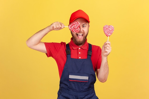 Operaio in uniforme blu con gustose caramelle zuccherate e occhi coprenti con lecca-lecca a forma di cuore