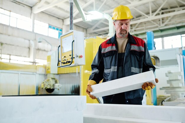 Operaio in uniforme che mette un pezzo di pietra sulla macchina per il taglio durante il suo lavoro in pianta