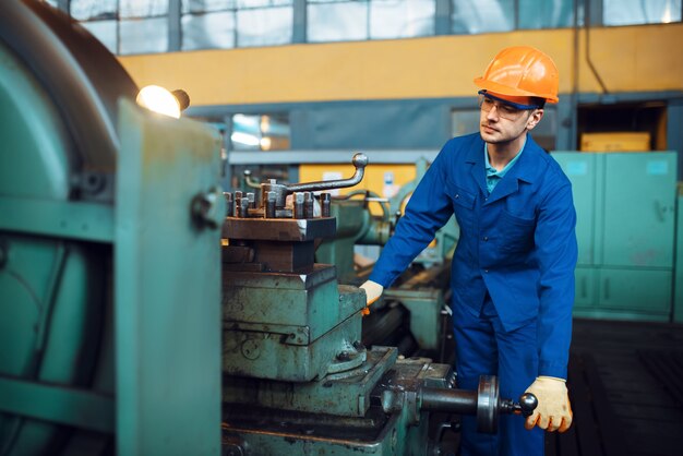 Operaio in uniforme e casco lavora al tornio, fabbrica. Produzione industriale, ingegneria della lavorazione dei metalli, produzione