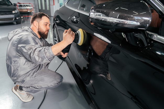 Operaio lucidatura auto con smerigliatrice speciale e cera da graffi presso la stazione di servizio auto