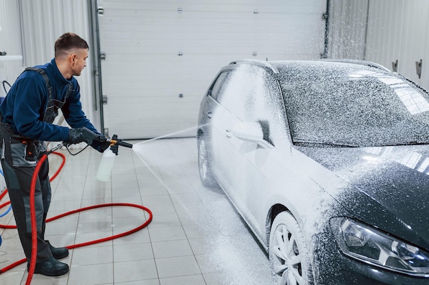 Operaio maschio in uniforme che lava la nuova automobile moderna che ricoperta di sapone Concezione del servizio