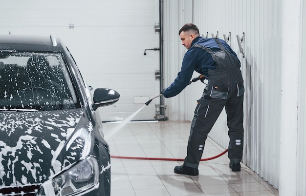 Operaio maschio in uniforme che lava la nuova automobile moderna che ricoperta di sapone Concezione del servizio