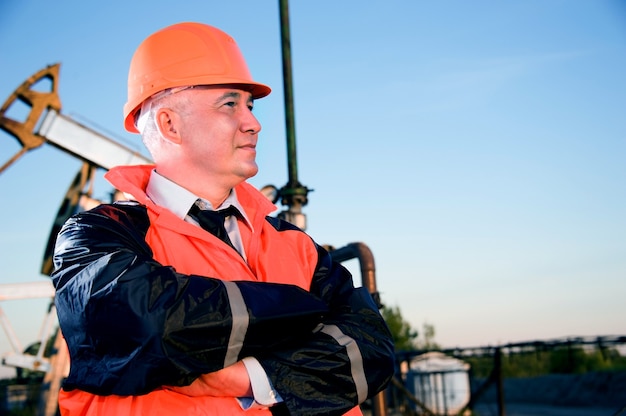 Operaio petrolifero in uniforme arancione e casco sullo sfondo della presa della pompa e del cielo blu.