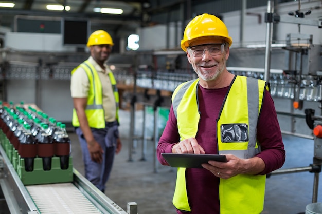 Operaio sorridente con la compressa digitale che sta vicino alla linea di produzione