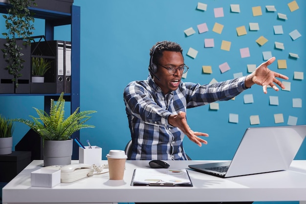 Operatore di call center arrabbiato pazzo che grida di rabbia mentre parla con il cliente. Agente di telemarketing furioso che urla al laptop mentre indica in modo aggressivo il display nell'area di lavoro dell'ufficio.